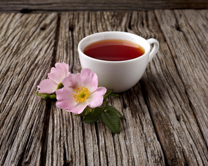 Rosehip flowers and cup of healthy tea, herbal medicine. A cup of  tea with rosehip on the wooden background