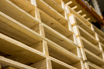 Light wood cargo pallets stacked high in a dirty factory neatly and cleanly on red industrial shelfs. Well built commercial freight pallets used internationally in shipping and commerce storage.
