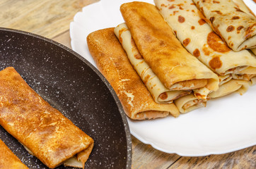 Thin pancakes with filling lie on a white plate. And part of thin pancakes with stuffing lies on pan. Cooking pancakes