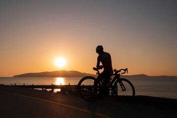 Fototapeta na wymiar Silhouette people ride a bicycle,bicycle rider watching the sunrise over the mountain at sea