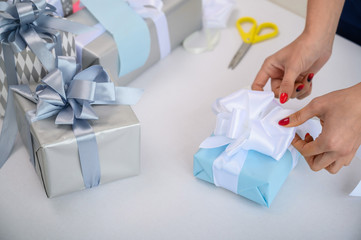 Woman wraps boxes with gifts for the new year. Female hands close-up. Prepares a surprise for mother's day. Wrapping paper and ribbon for birth. The designer is tying a bow.