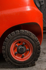 Red dirty forklift wheel in a factory with dirty tyres and dirty nuts and bolts. Vivid bright colours and dirty tyres. Covered in dust and grime