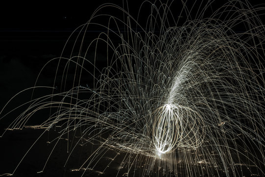 Night time image of steel wool long exposure ball photography on the beach with light trails flying every direction with chaos against the black background. Lots of lines mashed up into one creative 
