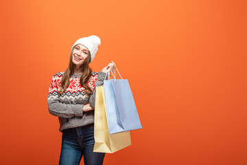 happy girl in winter outfit holding shopping bags on orange background