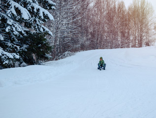 Cute Asian child boy playing on white snow  in Siberia, riding a snow scooter. Winter sport. Playing in the park outdoors.  With a smile of happiness. 