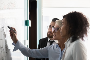 Diverse businesspeople write on board in office brainstorming