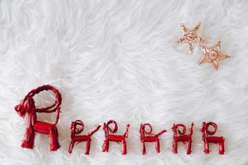 top view of Christmas composition on white snowy background for greeting card. Row of red straw reindeers with little straw stars