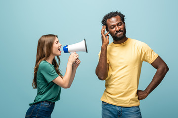 angry girl screaming in megaphone at african american boyfriend on blue background