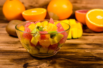 Salad with mango, oranges, grapefruit and kiwi fruits in a glass bowl on wooden table