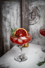 cocktail drink with blood orange and ice decorated with basil on white wooden stool