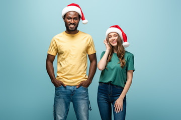 Fototapeta premium smiling interracial couple in santa hats on blue background