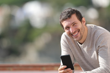 Happy adult man holding smart phone looks at camera