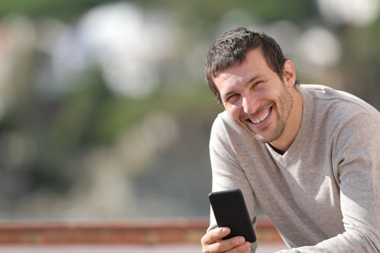 Happy adult man holding smart phone looks at camera - Powered by Adobe