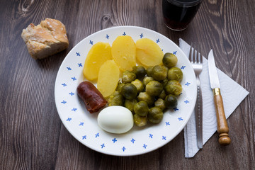 Plate with brussel sprouts, sausage, cooked potatoes and egg on a wooden table. Traditional Spanish food