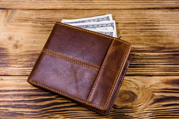 Brown leather wallet and one hundred dollar banknotes on the wooden background