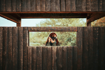 Young woman taking photos from wooden hut in the forest