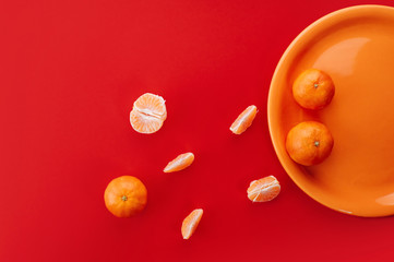 Tangerines on orange plate. Monochrome styled flat lay on bold red background.