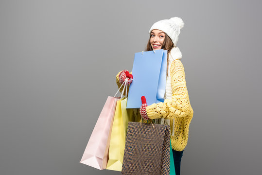 happy woman in winter outfit with shopping bags on grey background