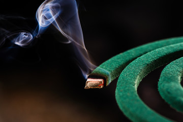 Burning green spiral mosquito repellent coil and red fire  with white smoke on dark background.