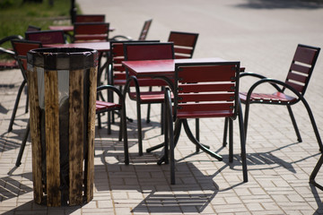 Outdoor bar. Wooden trash bin. Red tables and chairs in a summer cafe on the alley.