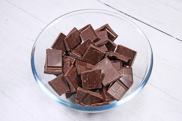 Dark chocolate in a glass bowl on white wood background