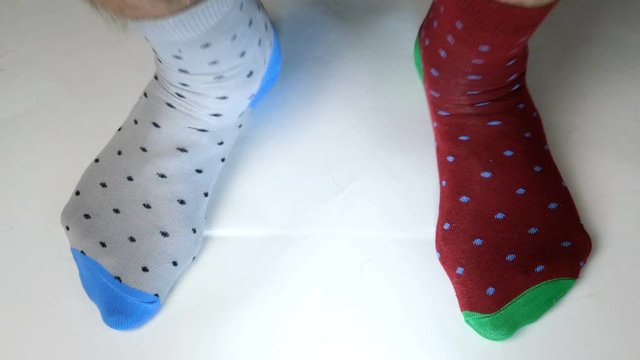 Human legs in fashionable socks of different colors move on white solid surface, jump on spot. Maybe he is dancing, doing sports or fitness. Close-up.