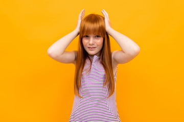 red-haired smiling beautiful girl in a T-shirt grimaces looking at the camera on a yellow background © Ivan Traimak