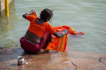 Life on the Ganges: Low caste untouchable indian woman washing a bright orange sari in t he holy river Ganges. Poverty in India.
