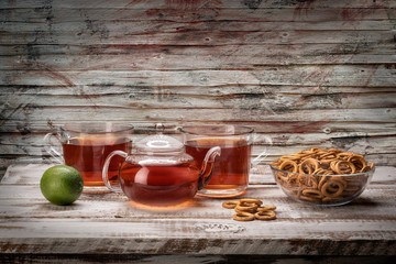 Still life food on a bright table of boards glass teapot and mugs with tea and a plate with dried...