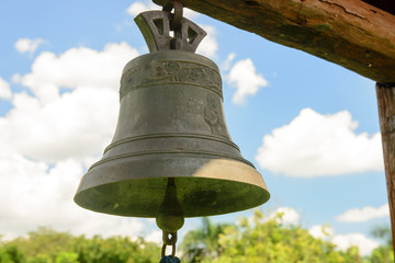 copper bell hanging with blue sky and clouds in the background