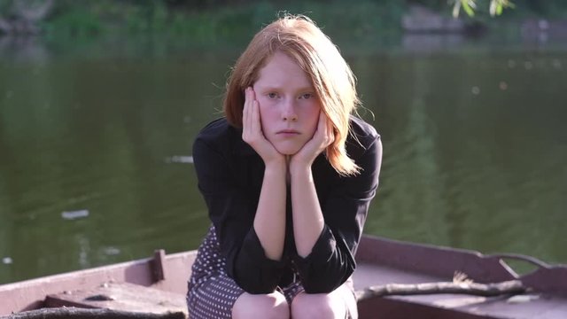Beautiful ginger girl sitting sad in a rusty boat. Butterfly nearby fly away