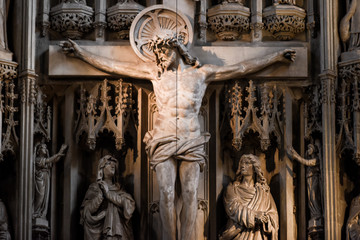 Jesus Christ on the cross in a cathedral or church interior surrounded by ornate stone carvings