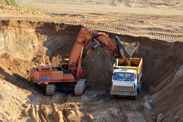 Fototapeta na wymiar Excavator developing the sand in the opencast and loading it to the heavy dump truck. Processing of loose material in mining quarry. Drill, breaking, processing plant, crushing and screening - Image