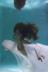 Beautiful girl swims underwater with long hair. Blue or gold background like gold. The atmosphere...