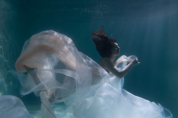 Beautiful girl swims underwater with long hair. Blue or gold background like gold. The atmosphere...