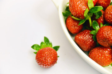 Freshly harvested red strawberries in ceramic bowl with white background.