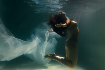 Beautiful girl swims underwater with long hair. Blue or gold background like gold. The atmosphere...