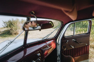 Smiling and in love newlyweds hug, and are reflected in the rear view mirror of an expensive car in...