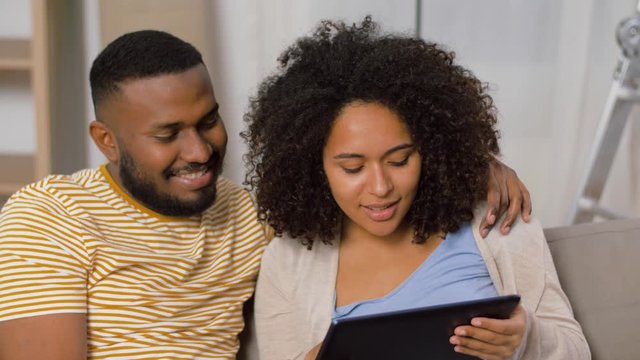mortgage, people and real estate concept - happy african american couple with tablet pc computer sitting on sofa at new home