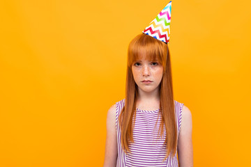 red-haired girl with a holiday cap looks at the camera on a yellow background
