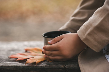 Hands of little girl holds a thermos cup of tea in the park with the copy space for text