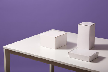 Close up of white paper carton boxes on table isolated over lilac background, three blank cases on desk, studio shot of shells, copy space for advertisment or promotional text, e commerce concept.