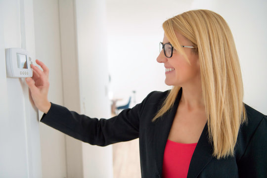 A Smiling Business Woman Adjusting Thermostat On Home Heating System