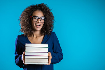 African student with glasses on blue background in the studio holds stack of university books from...