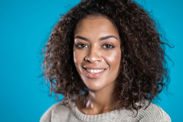 Attractive african american woman with afro hair smiling to camera over blue wall background. Cute mixed race girl's portrait