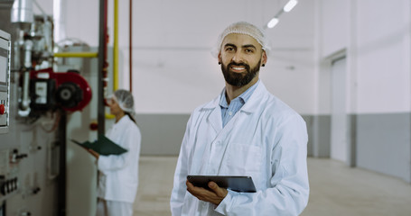 In the morning two beautiful engineers in manufacturing industry check the industrial machine and make some notes on the electronic tablet