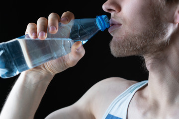 a skinny sportsman with a plastic bottle with pure water while workout