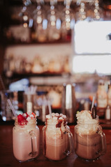 Line up of strawberry, caramel and chocolate milkshakes with marshmallows. Concept of restaurant, drinks and hospitality. Free space for text. Selective focus on the glasses.