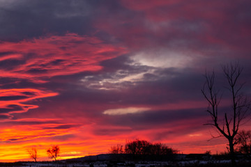 Red-blue sunset with dark clouds on the outskirts of the village. Dark winter rural silhouette with a beautiful sunrise. Artistically blurry