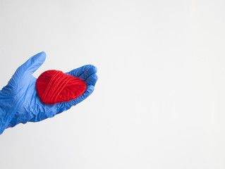 a hand in a blue glove holds a red heart. Medical concept. Copy space